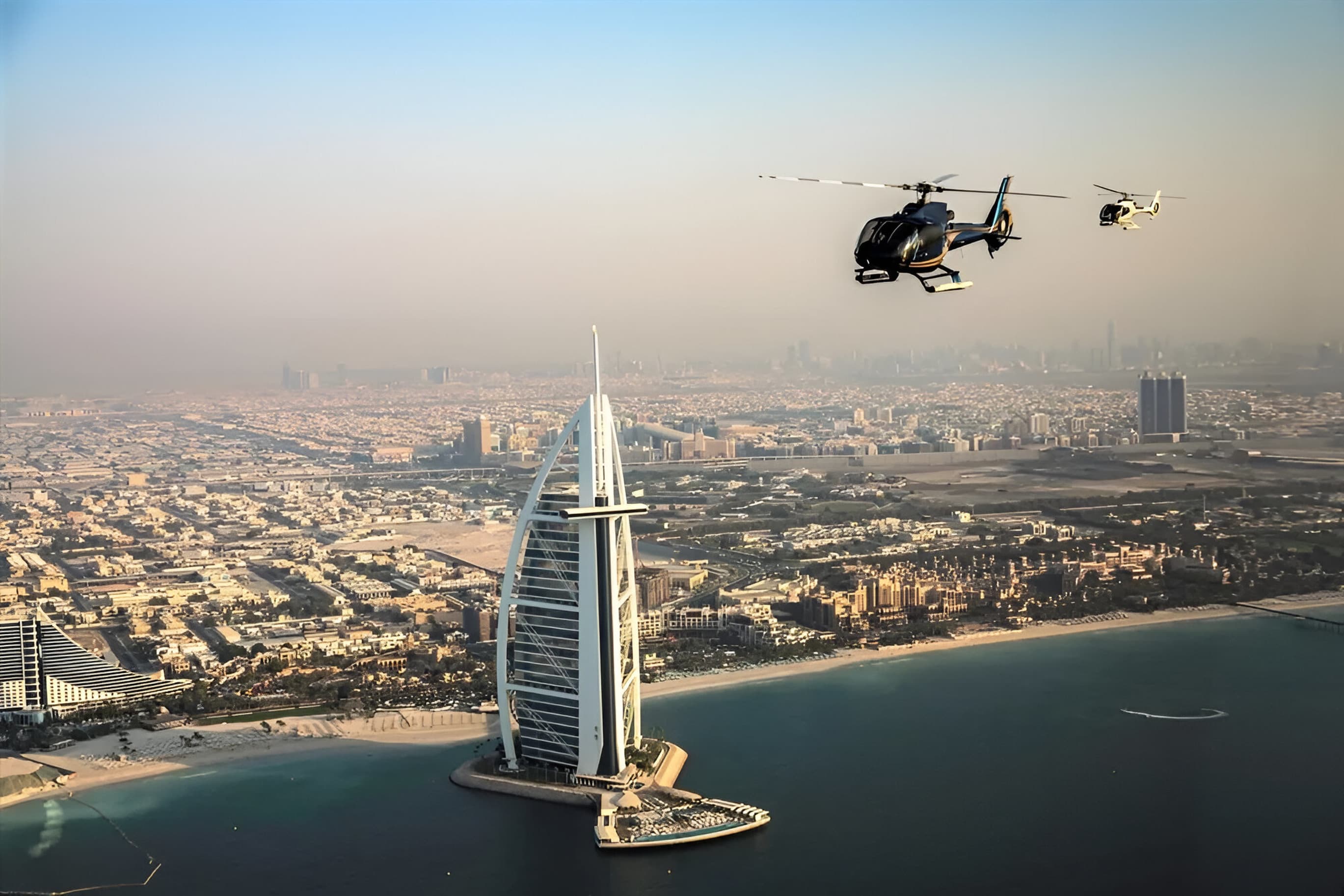 Two helicopters fly past the iconic Burj Al Arab hotel above the Dubai coastline.